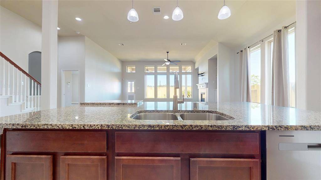 This photo showcases a spacious, open-concept living area viewed from the kitchen island. It features granite countertops, modern pendant lighting, and large windows that provide ample natural light.