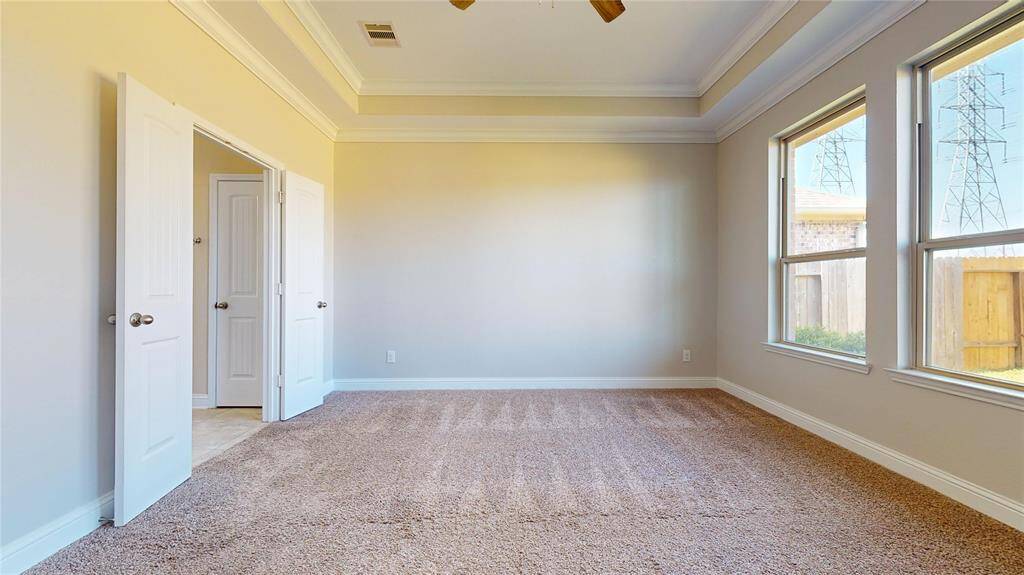 The Primary Bedroom features a spacious layout with two large windows for natural light, and elegant tray ceilings. It includes a doorway leading to an adjacent bathroom area, enhancing functionality and flow.
