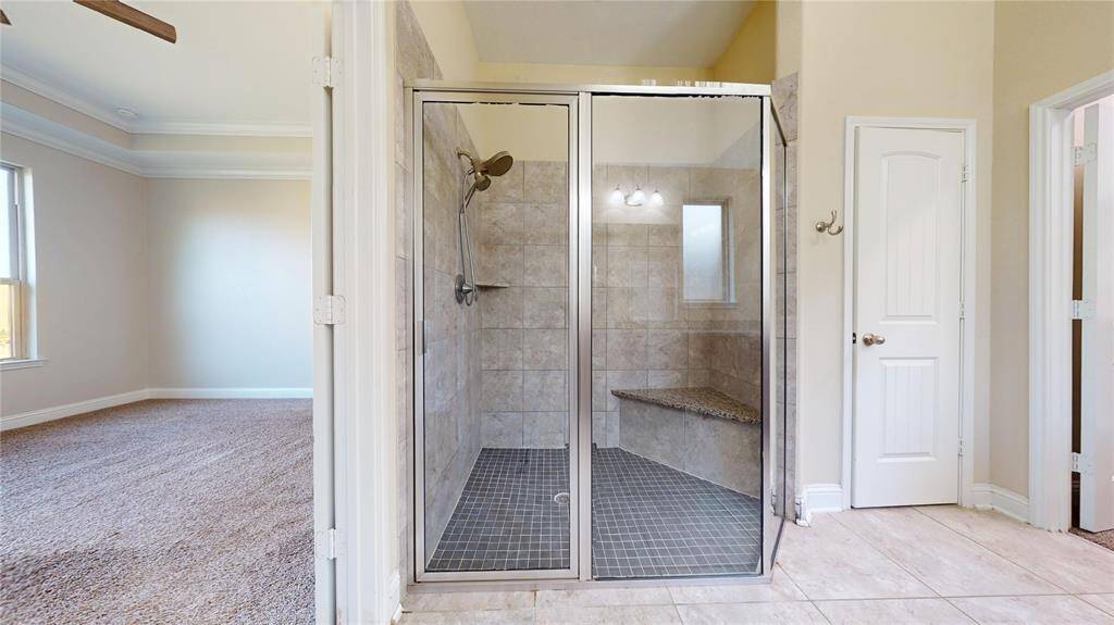 This photo show the Primary bathroom glass-enclosed walk-in shower with elegant tile work and a built-in bench. Toilet room and large closet to the right.