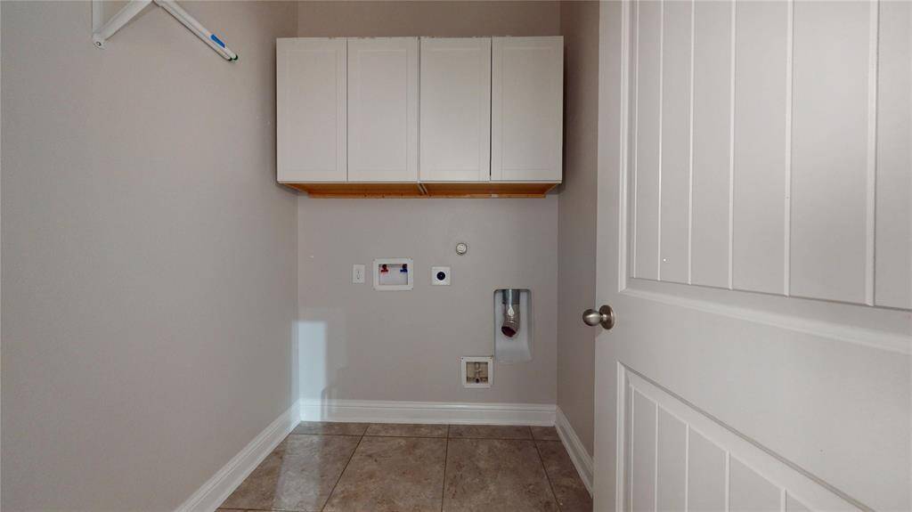 This is a laundry room with tile flooring, featuring upper white cabinets for storage, and connections ready for a washer and dryer.