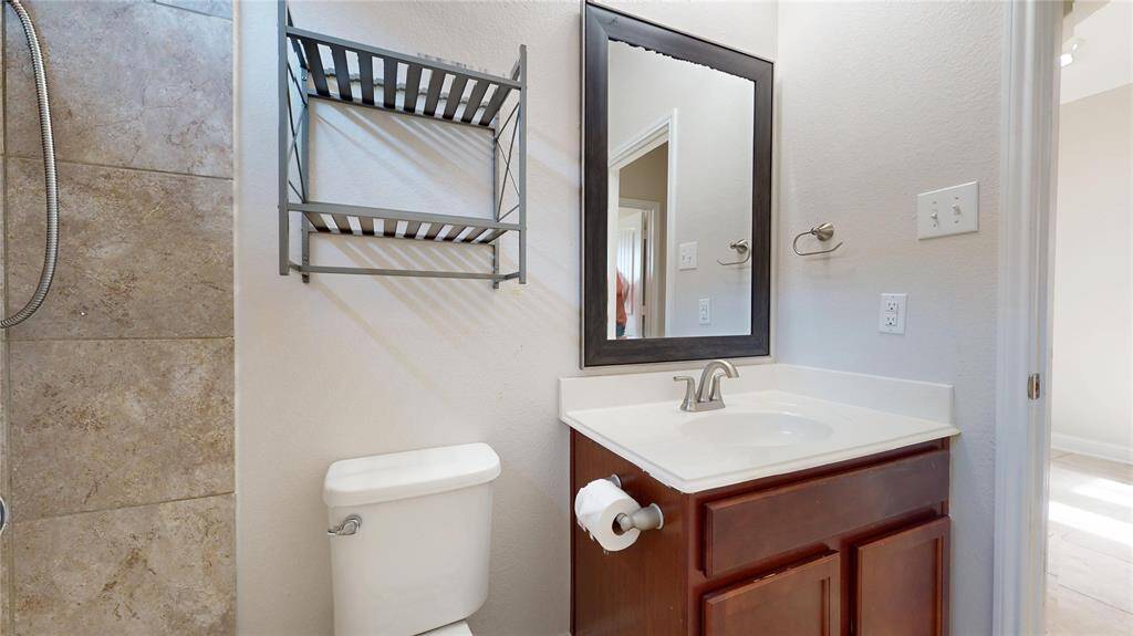 This Guest bathroom features a tiled shower area, a modern sink with a dark-framed mirror, and a storage rack above the toilet.