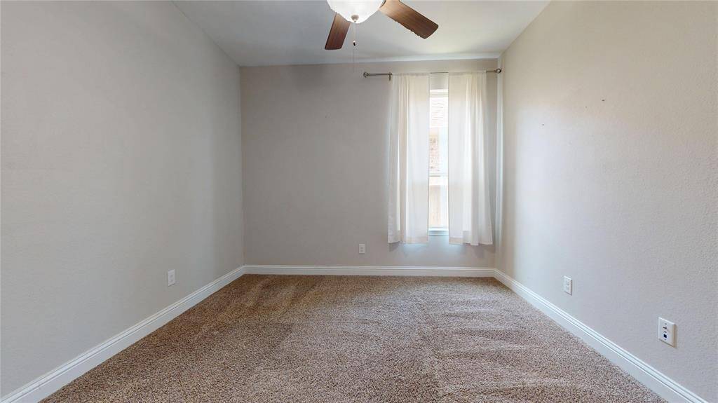 Guest bedroom #3 with neutral-colors, featuring a window with sheer curtains. It includes a ceiling fan and has ample natural light.