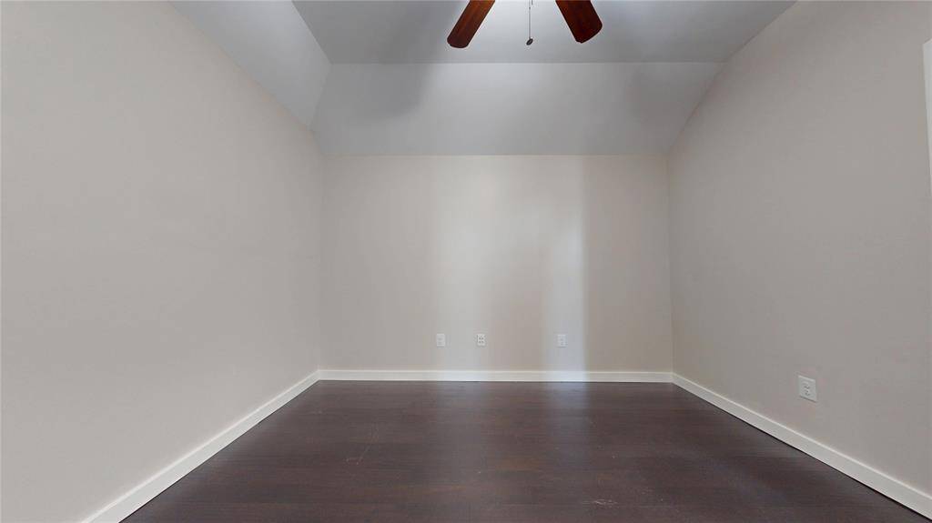 This photo shows the extra room that is upstairs with dark hardwood floors and ceiling fan that is centrally mounted. This is a perfect room for a study, storage or whatever else you may need.