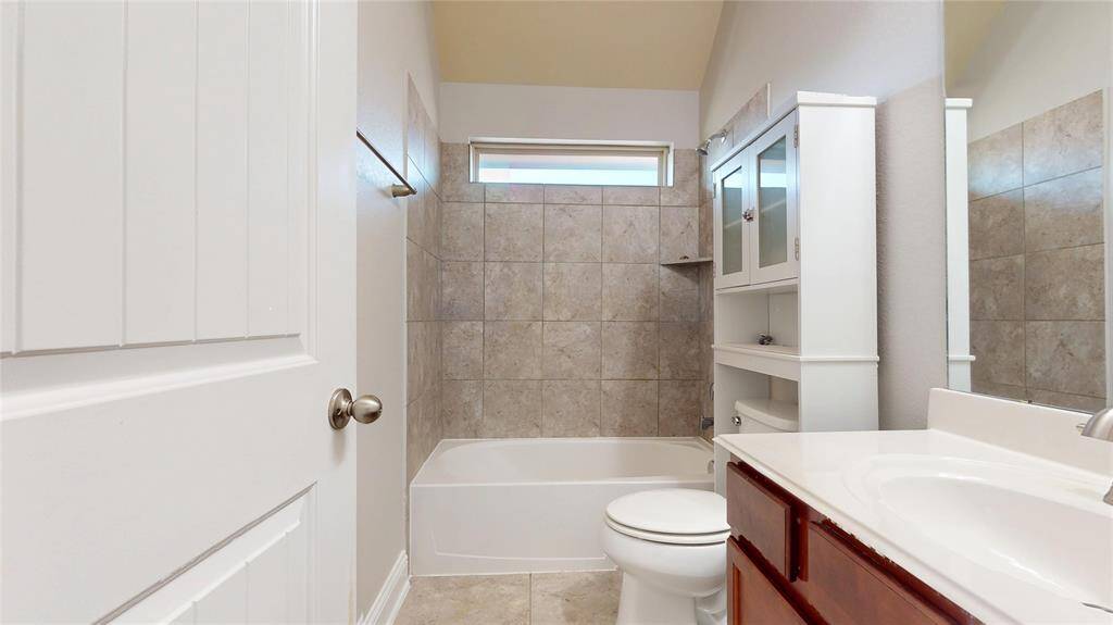 This upstairs guest bathroom features a clean and modern design with tiled walls surrounding the bathtub, a built-in cabinet for storage, and a sleek vanity with a mirror.