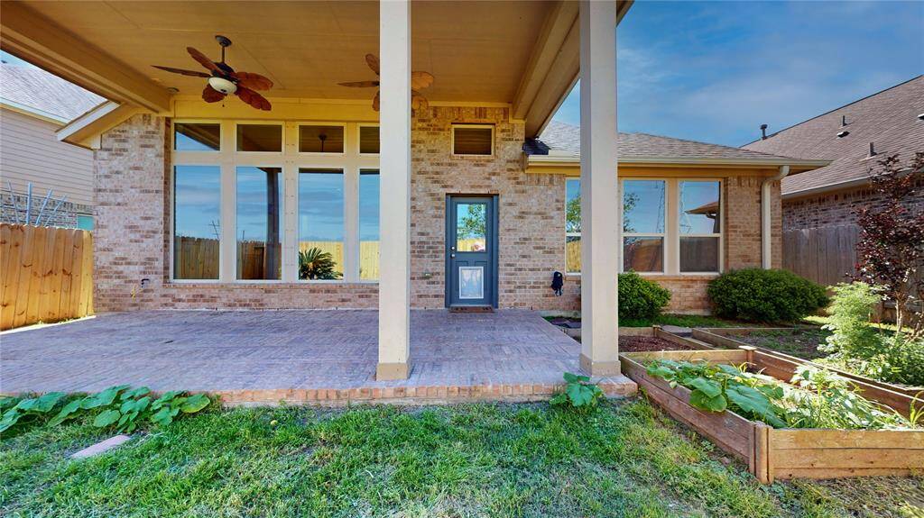This photo showcases a spacious backyard patio with a brick surface, featuring ceiling fans for comfort. The large windows offer a view into the home, providing a seamless indoor-outdoor connection.