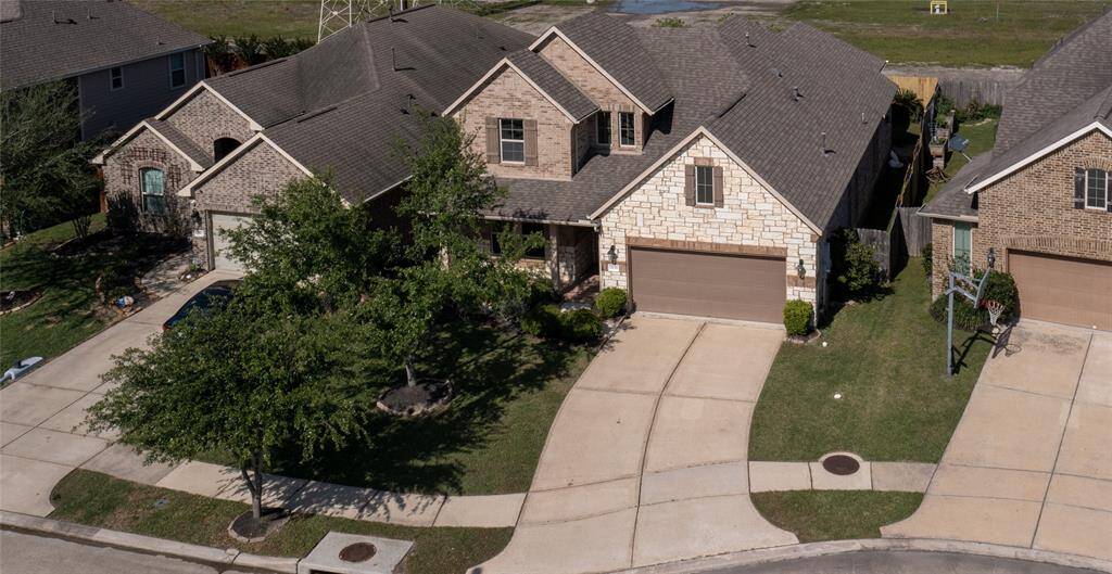 This photo shows a charming two-story brick and stone home with a two-car garage and a well-maintained front yard. Located in a quiet neighborhood, the house features a spacious driveway and is surrounded by similar homes, offering a welcoming community feel.