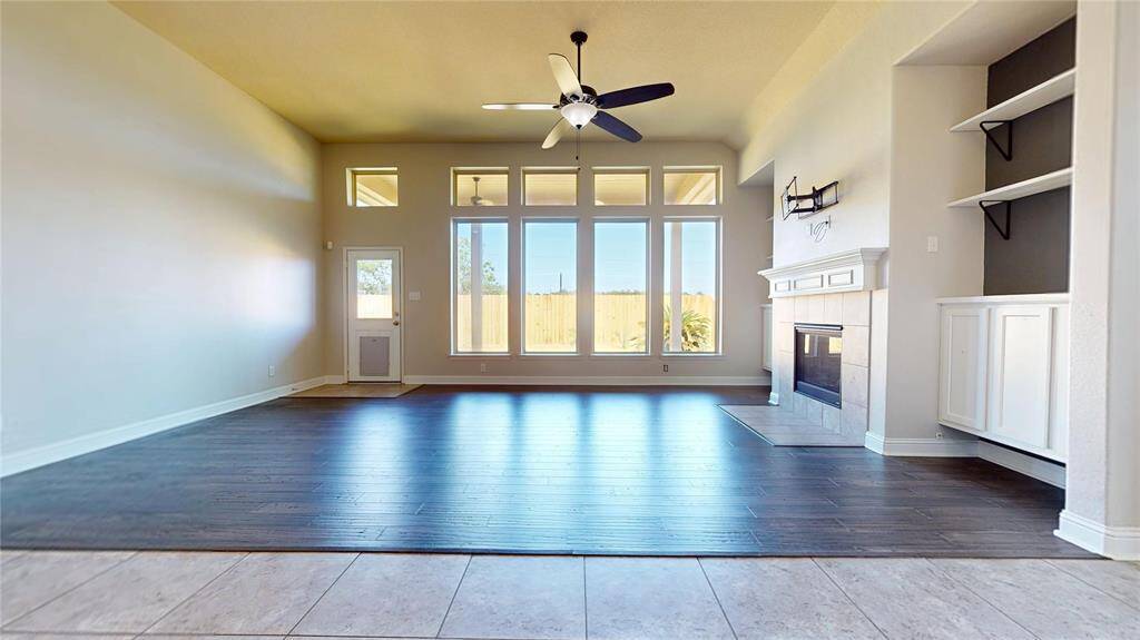 This spacious living room features large windows for abundant natural light, a ceiling fan, and elegant bambo hardwood flooring. It includes a cozy fireplace with built-in shelving and cabinetry, perfect for storage and display.