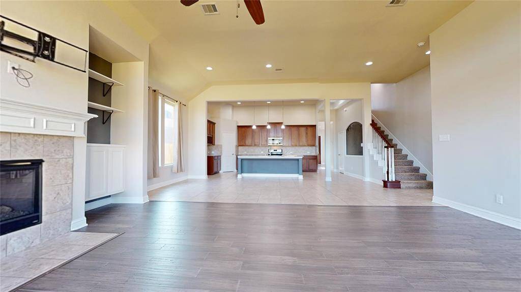 This spacious open-concept living area features a modern kitchen with a large island, a cozy fireplace, and elegant wood and tile flooring. The staircase leads to the upper level of the home. Perfect for comfortable living and entertaining.