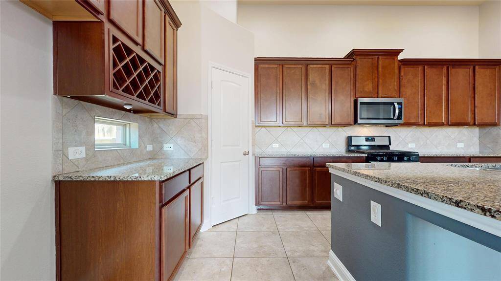 This kitchen features elegant wooden cabinetry with plenty of storage, granite countertops, and a built-in wine rack. It includes modern stainless steel appliances and a tiled backsplash.
