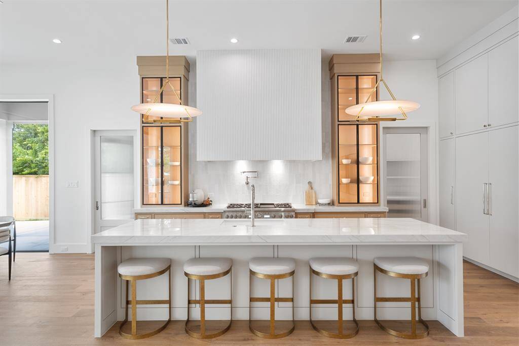 This kitchen features exquisite custom cabinetry with elegant glass doors, showcasing fine craftsmanship and attention to detail. Under-cabinet lighting highlights the shelves, creating a warm, inviting glow that beautifully accents the display items inside.