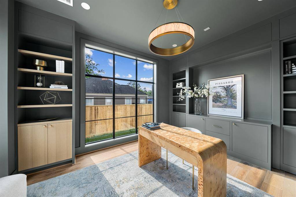 This moody office features oversized windows that allow soft, natural light to pour in, creating a balanced, inviting atmosphere. Custom bookshelves line the walls, offering both style and storage, while a "hidden" closet seamlessly blends into the design, adding an element of surprise and functionality.