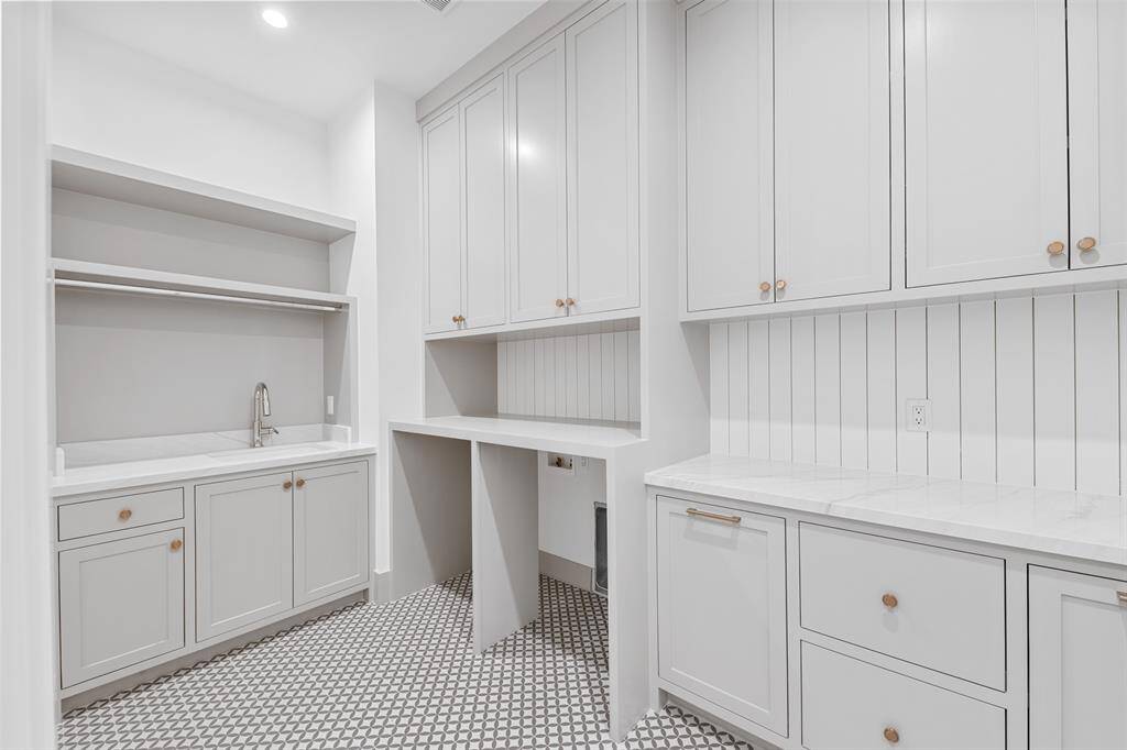 This spacious upstairs laundry room features custom cabinetry for ample storage and a convenient sink, making laundry tasks more efficient and organized.