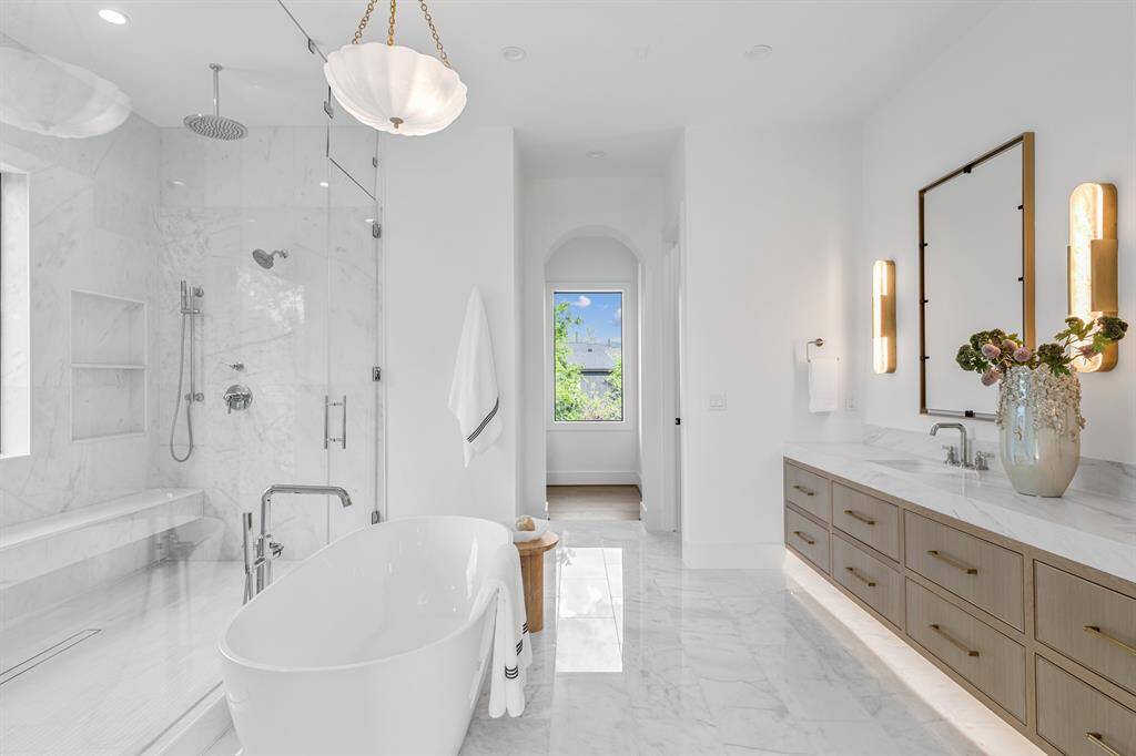 This luxurious primary bathroom features a double canity with custom cabinetry that combines both style and functionality underlighting. The spacious walk-in shower and elegant standalone bathtub create a spa-like atmosphere.
