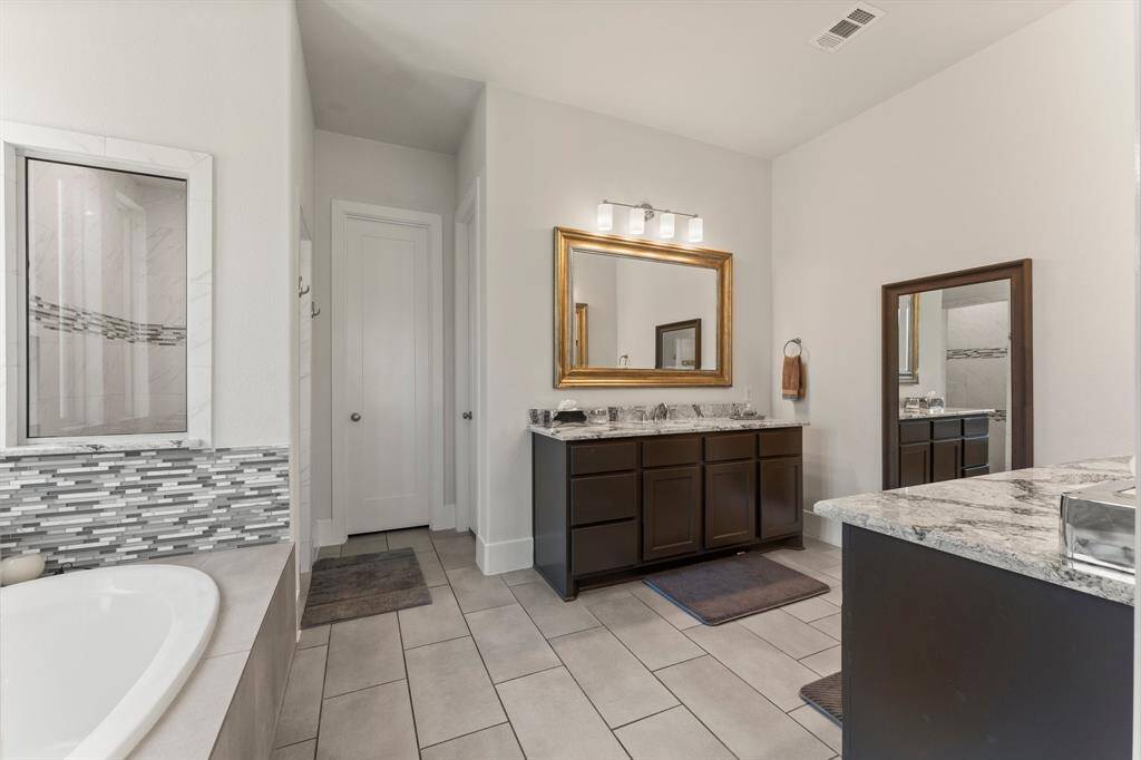 The spa-inspired primary bath features dual granite-topped vanities, framed mirrors, and a spacious layout that offers privacy and ease of use.