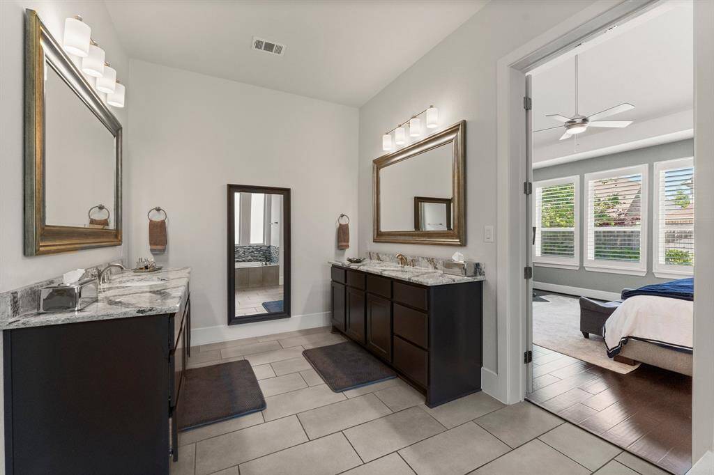 Spacious and elegant primary bath featuring separate vanities with granite counters, framed mirrors, and modern lighting. The layout provides privacy and function, with a large soaking tub, walk-in shower, and a view into the serene primary suite.