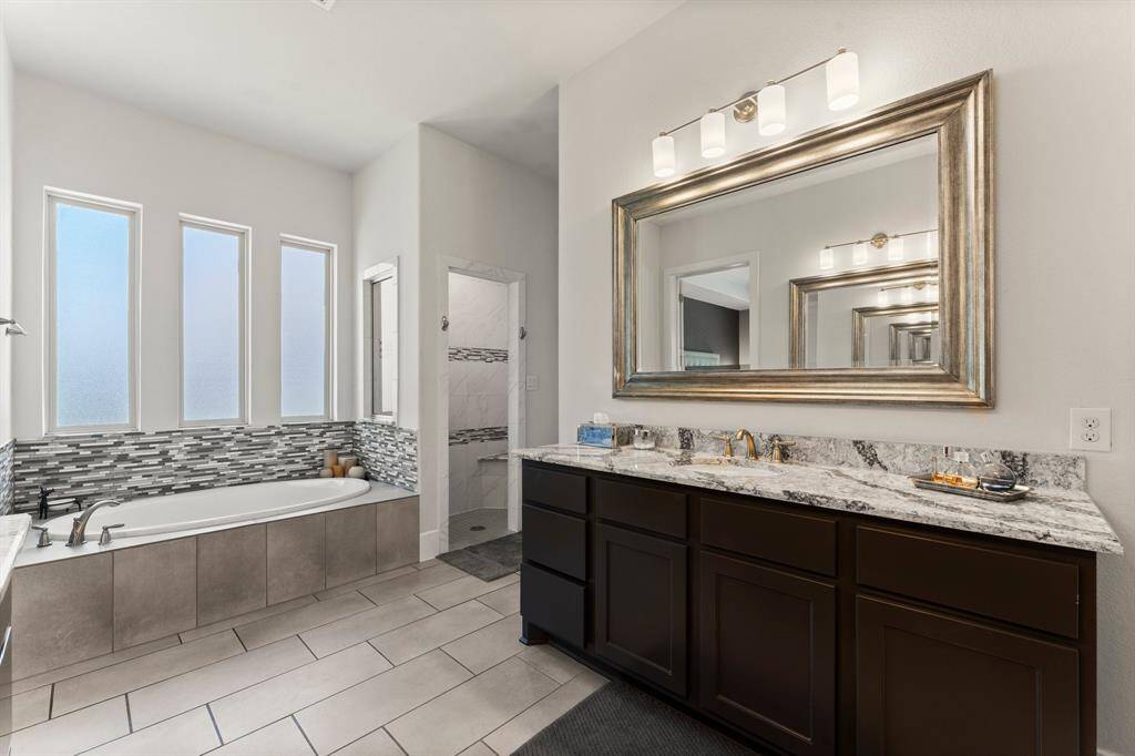 A luxurious soaking tub is framed by frosted picture windows and accented with mosaic tile, paired beautifully with a walk-in shower and sleek finishes.