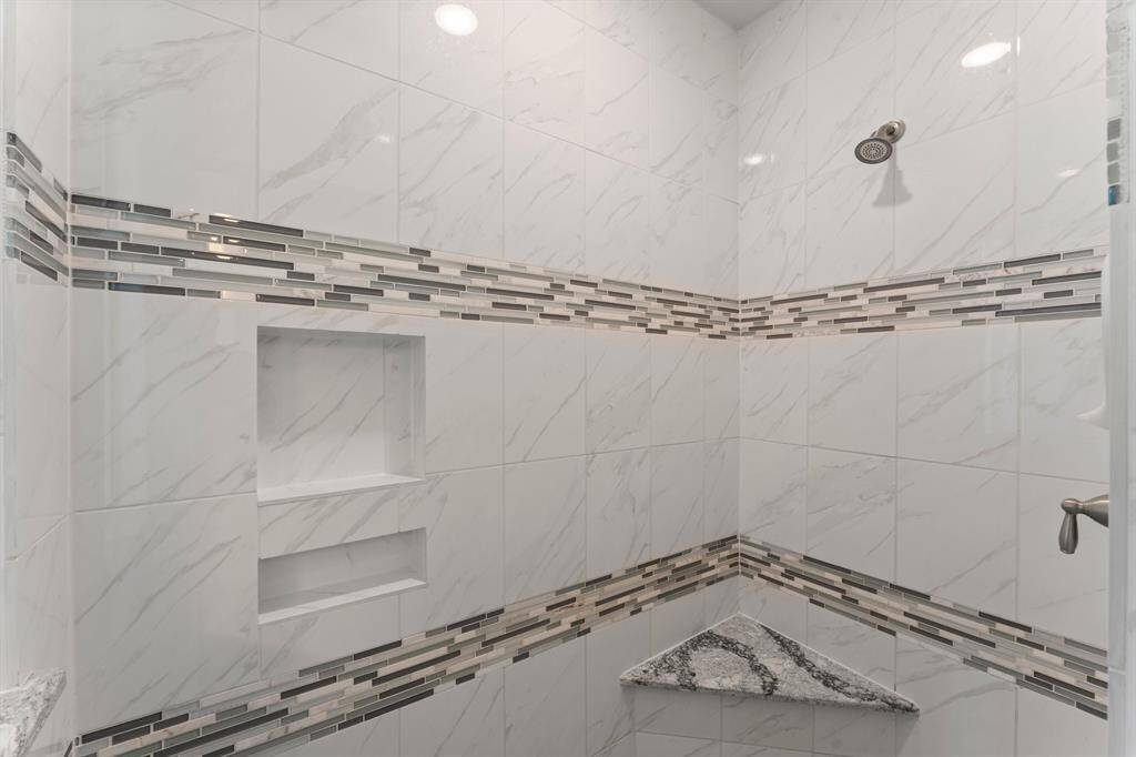 A closer look at the oversized shower reveals marble-look tile, dual niches, and designer mosaic accents with a built-in bench—equal parts stylish and functional.