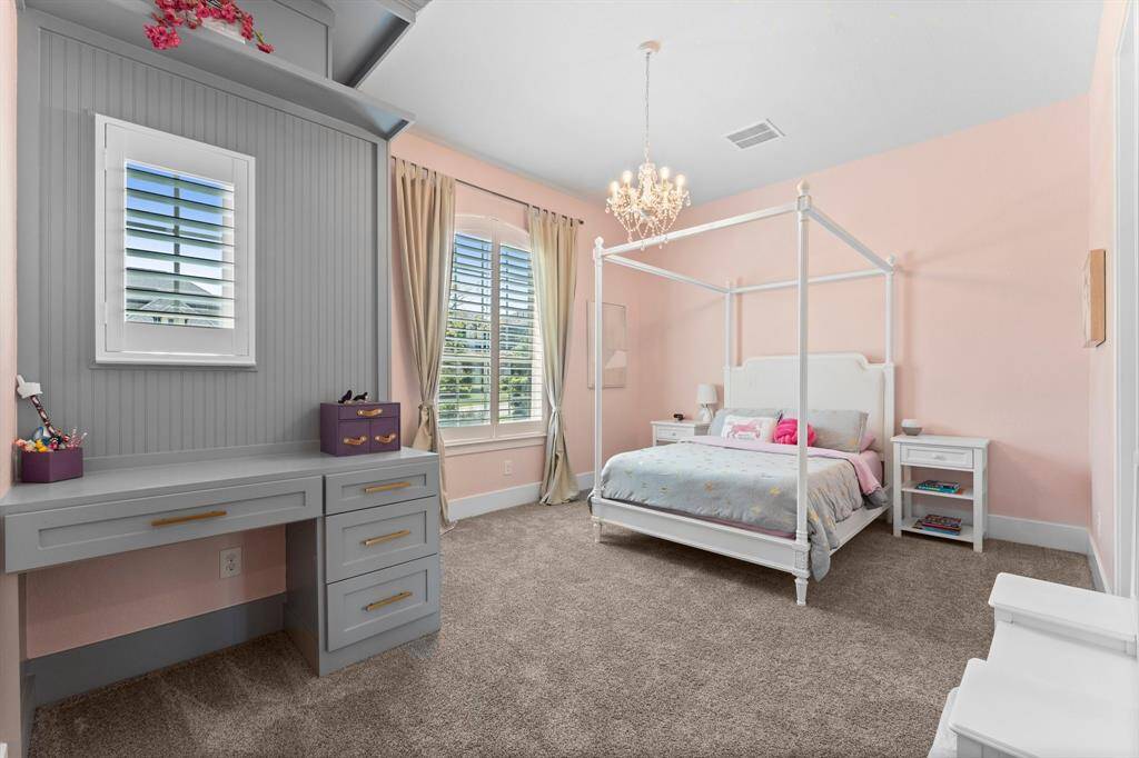One of the spacious secondary bedrooms is ideally located on the first floor, complete with a custom built-in desk, storage shelving, plantation shutters, and plush carpeting.