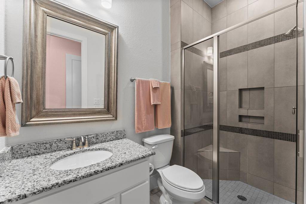 This private en suite bath features modern tilework, a walk-in shower with glass enclosure, and granite countertops with a framed mirror.