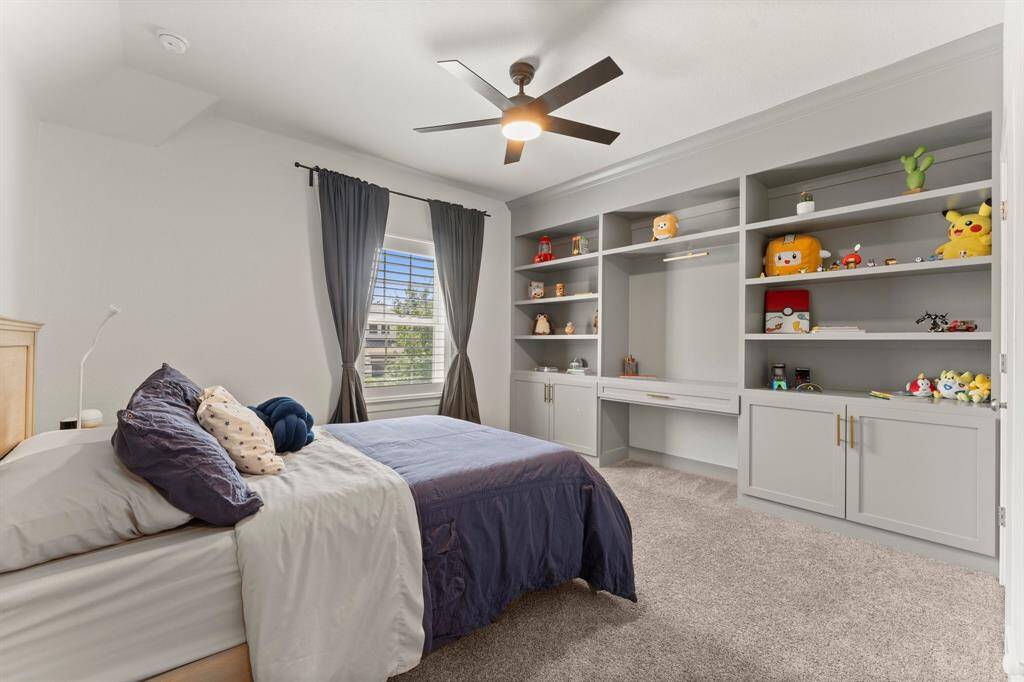 Generously sized secondary bedroom with custom built-ins including shelving, cabinets, and a desk—perfect for study or display.