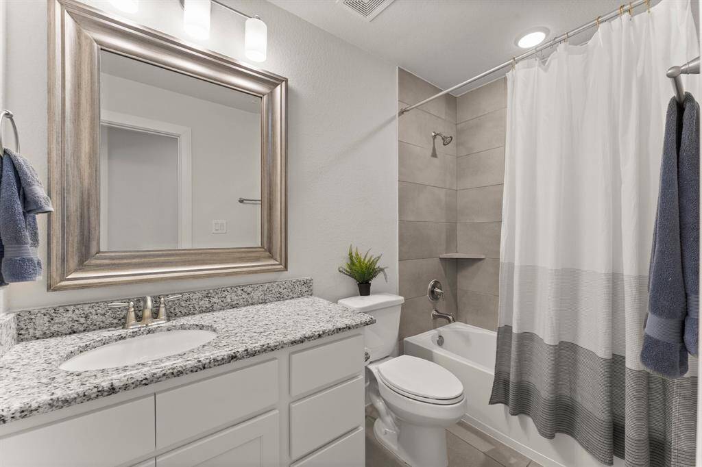 Stylish full bathroom with granite vanity and a combination tub/shower surrounded by contemporary tilework.
