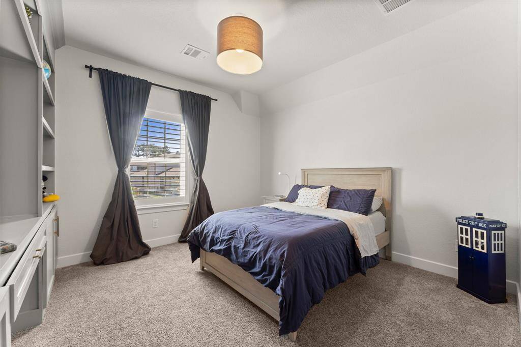Bright and airy secondary bedroom with plush carpeting and a large window fitted with plantation shutters.