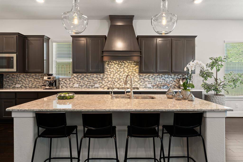 Sleek pendant lighting highlights the oversized island, perfect for casual dining or entertaining. The stylish vent hood and detailed backsplash elevate the space with modern elegance.