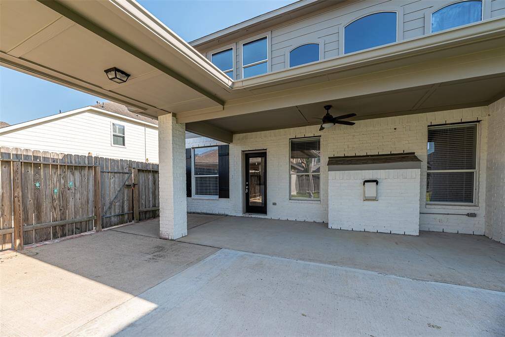Backyard of home has covered patio with ceiling fan and covered walk way to detached garage.
