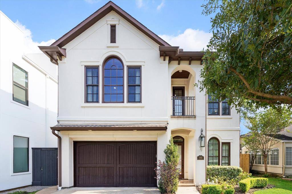 This is a stately two-story home, featuring arched windows, balcony, gas lamp, and a covered front porch. It includes a two-car garage and is surrounded by well-maintained landscaping which contributes to its elegant front elevation.