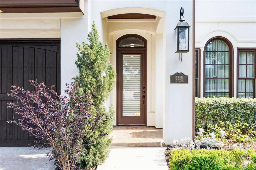 The covered entryway with a modern glass door is flanked by neat landscaping and features a lantern-style gas light fixture.
