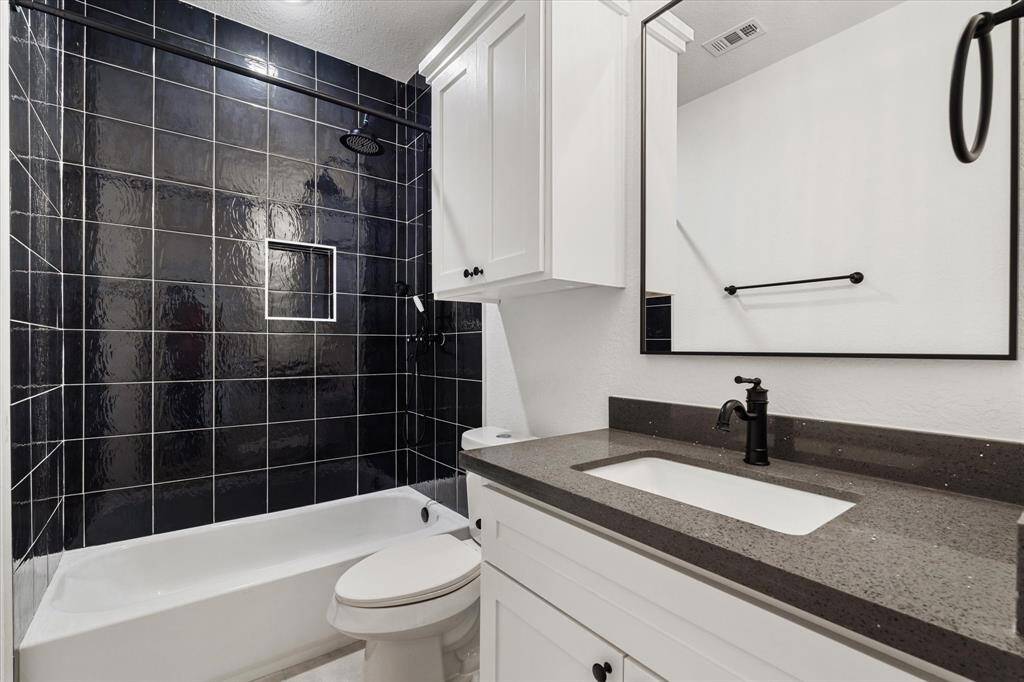 The guest bathroom boasts a shower-tub combo with black tile extending to the ceiling, a built-in soap niche, sleek black fixtures, and a convenient cabinet above the toilet.