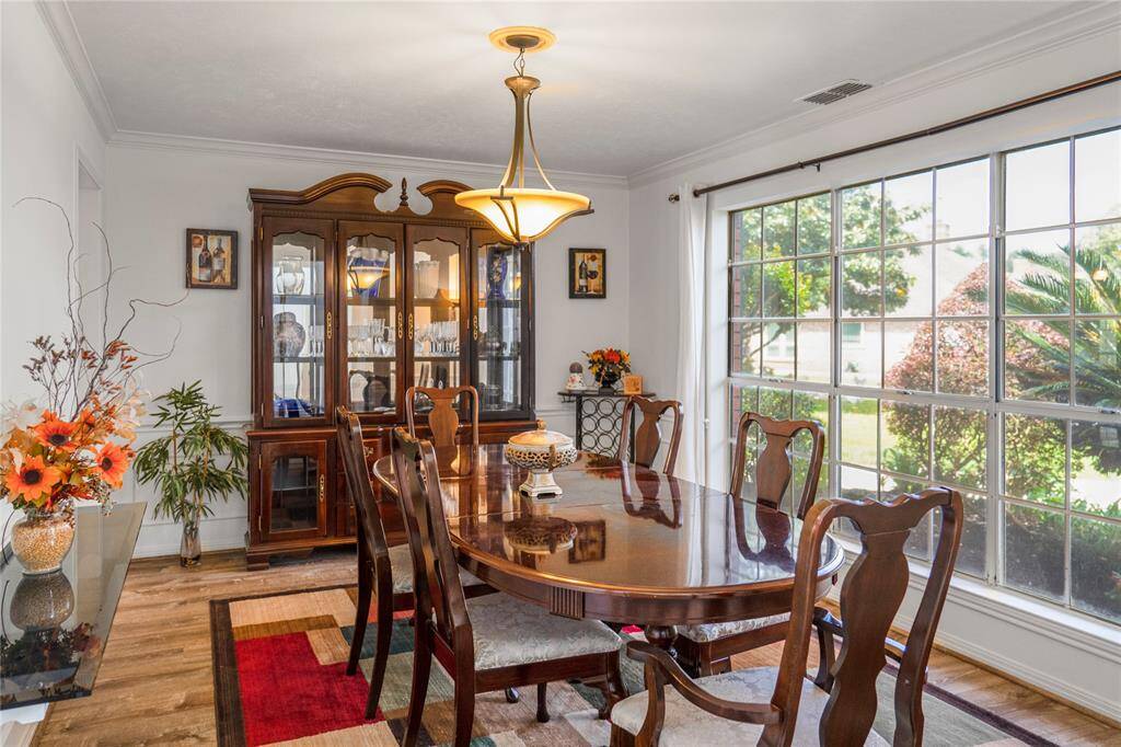 Elegant formal dining area overlooking a beautiful flower bed, with large windows that fill the space with natural light.
