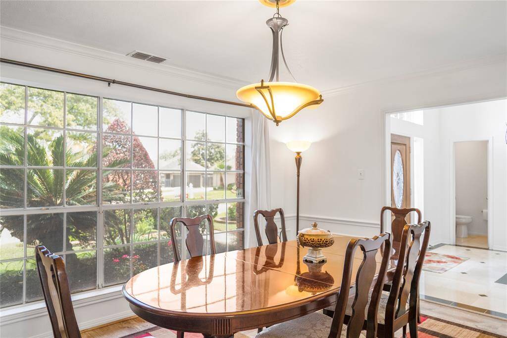 Elegant formal dining area overlooking a beautiful flower bed, with large windows that fill the space with natural light.