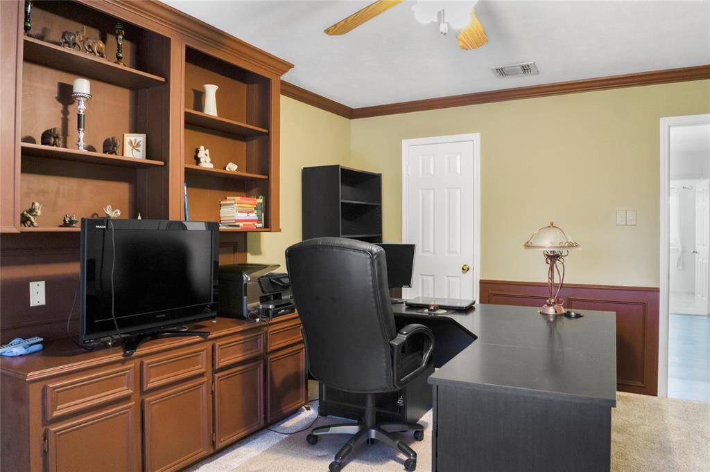 This well-lit home office features a large window with plantation shutters and built-in wooden shelves. It also includes a walk-in closet, making it suitable for use as an additional bedroom.