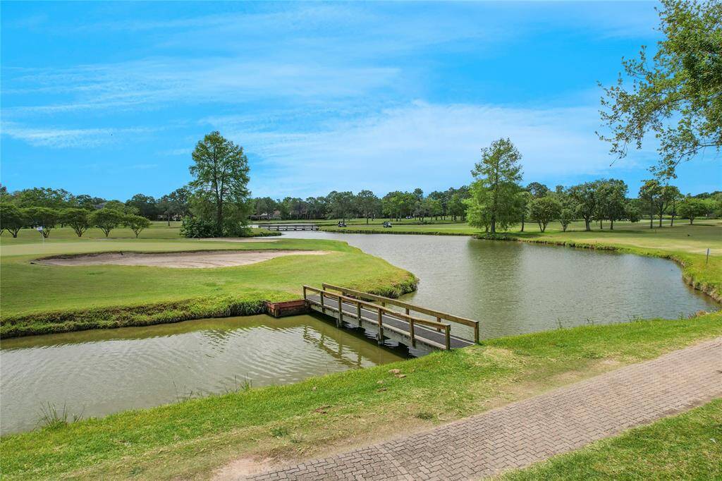 A serene golf course view with a small bridge over a pond, surrounded by lush greenery and trees, perfect for a homebuyer seeking a picturesque and tranquil setting.