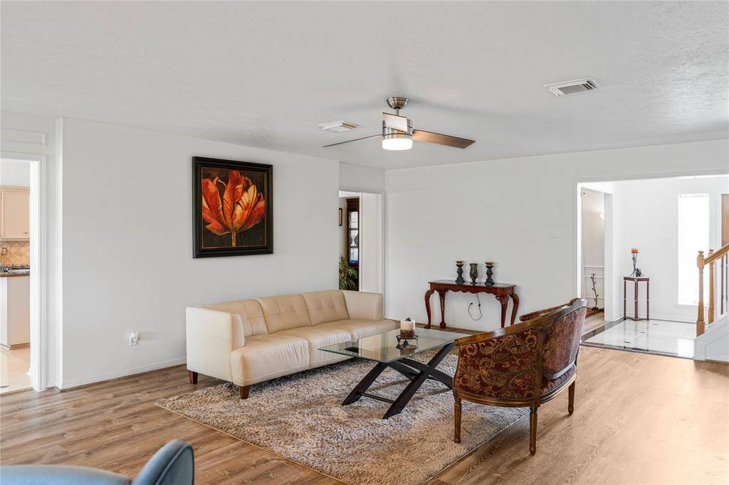 This living room is bright and spacious, featuring a modern ceiling fan, light hardwood floors, and large windows.