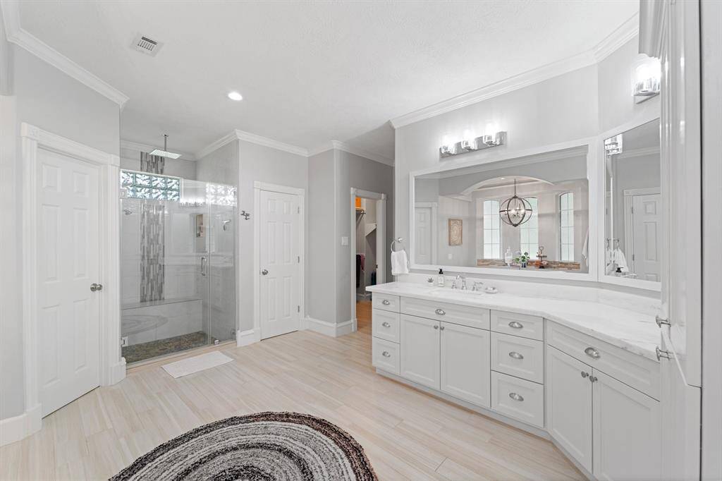 Primary bathroom features: two separate vanities, a lot of cabinet storage, framed mirrors, crown molding, and an oversized shower