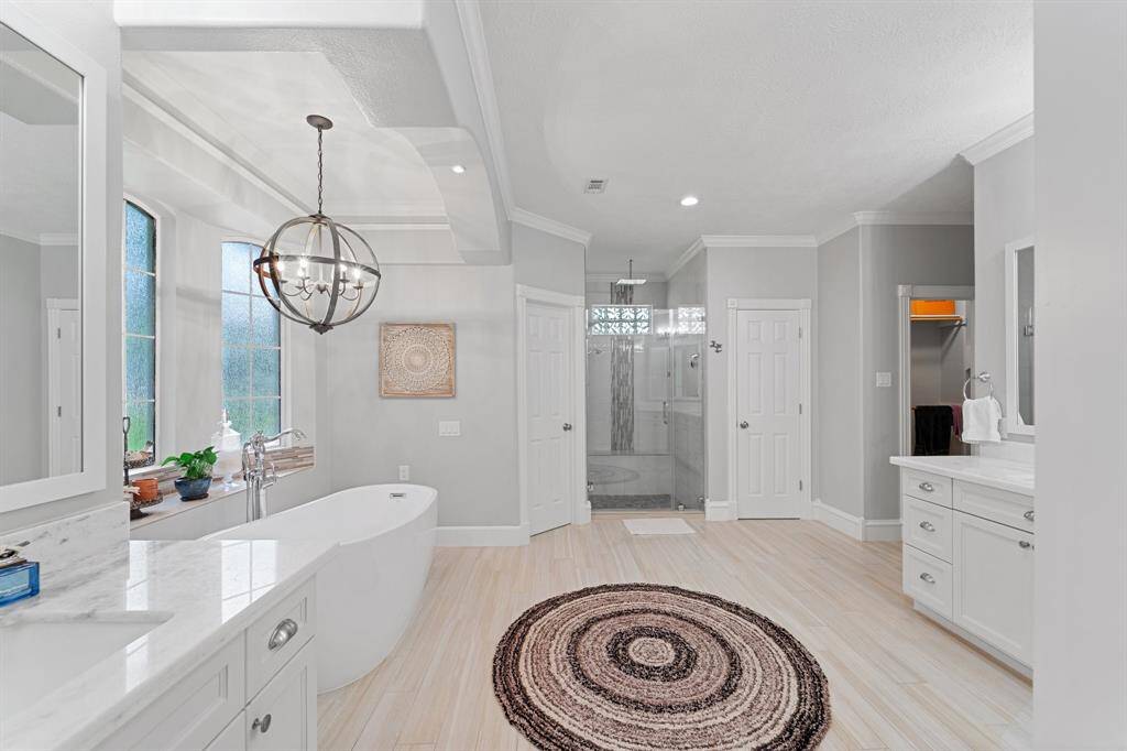 Renovated primary bathroom is complete with two separate vanities with sinks, a stand-alone soaking tub under a beautiful chandelier, oversized shower and walk-in closet.
