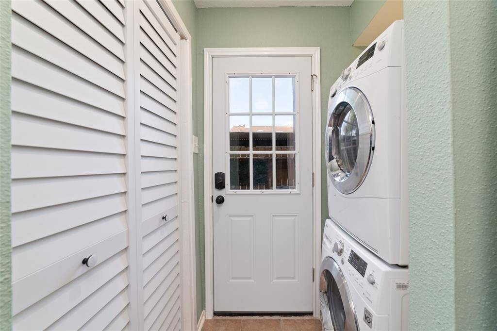 This efficient laundry room features a stacked washer and dryer, included in the sale, with adjacent louvered closet doors that provide extra storage. The soft green walls add a touch of calm to the space.