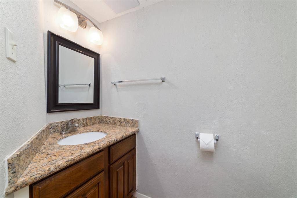 This half bathroom offers a sleek granite countertop with a built-in sink, complemented by a wooden vanity and a wall-mounted mirror.