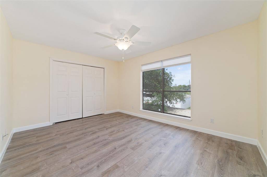The secondary bedroom offers light laminate flooring, neutral paint, and a ceiling fan for comfort. A large window fills the room with natural light and provides views of the outdoors, while a double-door closet offers ample storage space.
