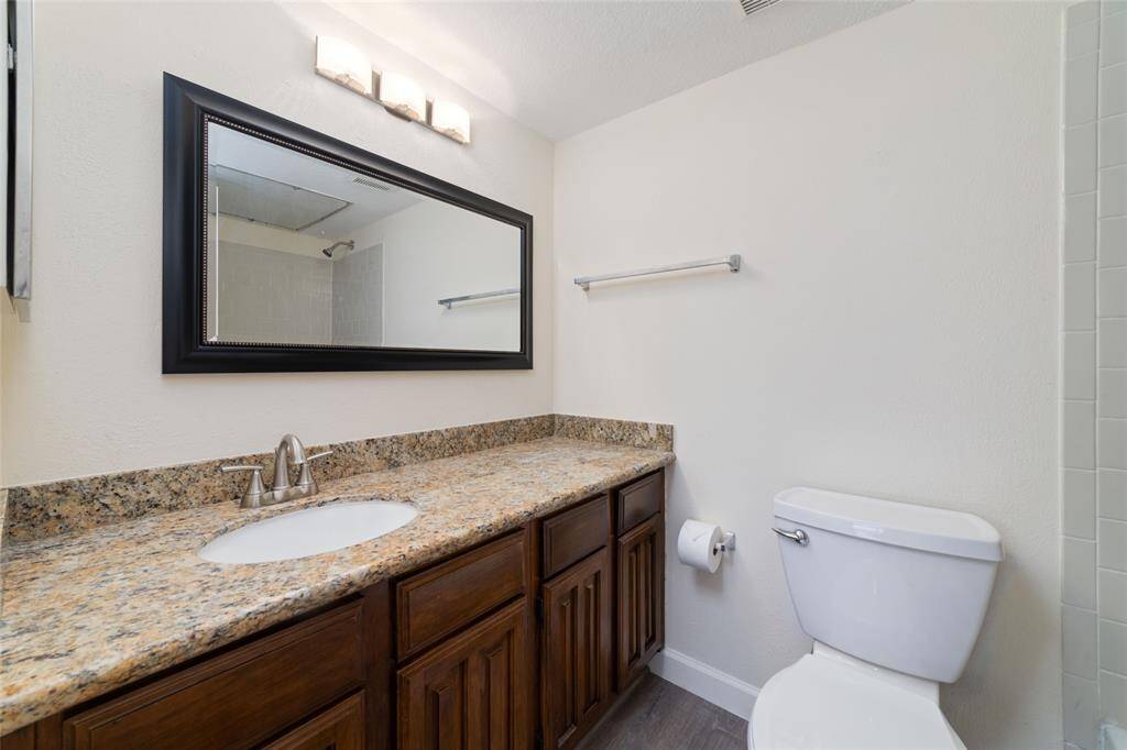 The bathroom has a granite countertop with a single sink, wood cabinetry, and a large framed mirror. A shower-tub combo and modern lighting add both style and functionality to the space.