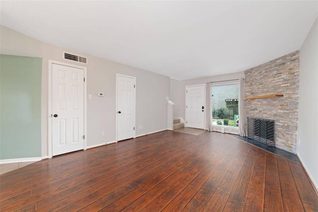 This spacious living room is filled with natural light from a large window that looks out the front of the home. One door reveals a cozy Harry Potter-style storage nook, while another leads to a convenient half bathroom.