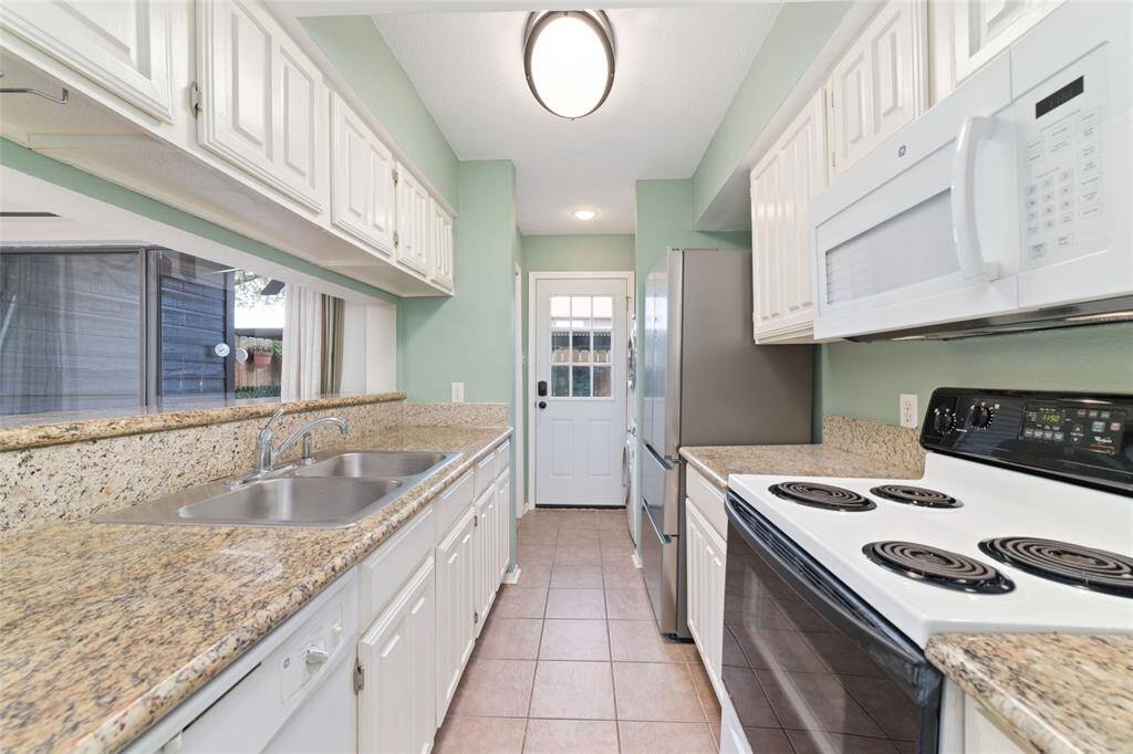 The galley-style kitchen is designed with granite countertops, white cabinets, and a stainless-steel refrigerator, offering a clean and efficient layout.