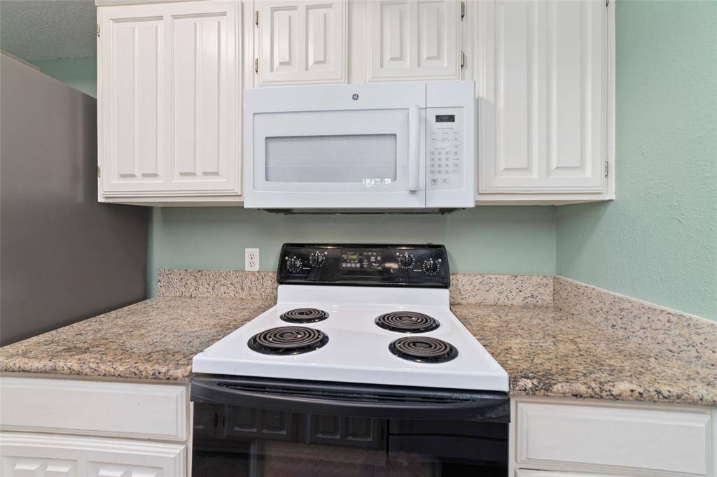 This kitchen boasts white cabinetry, a built-in microwave, and an electric stove. The  light green wall and granite countertops give the kitchen a refreshing vibe!