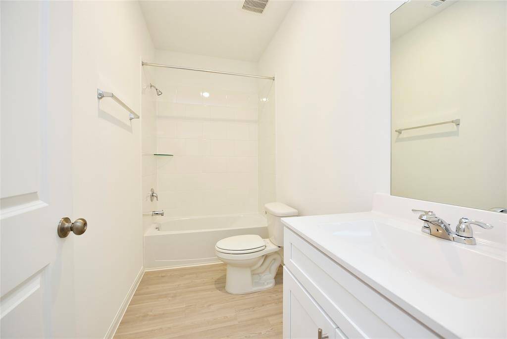 Secondary bath  tub shower combo with marble countertops and plank flooring.