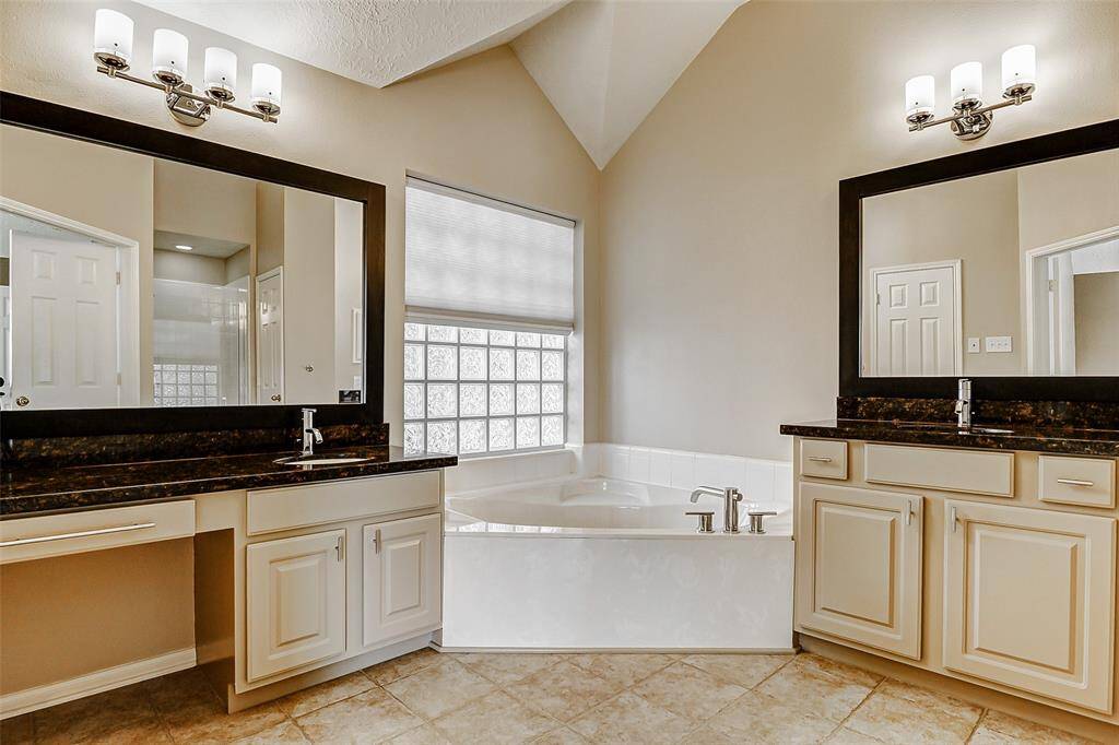 The beautiful primary bathroom offers a perfect blend of style and functionality, boasting double sinks, a garden tub, stunning granite countertops, huge mirrors, and a dedicated vanity area.