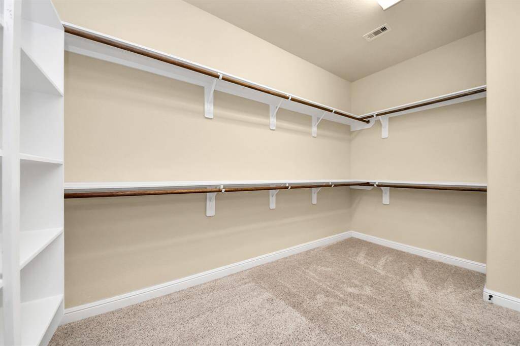 The primary suite includes a walk-in closet with ample shelving and hanging space, featuring neutral walls and carpeted flooring for a clean, organized look.