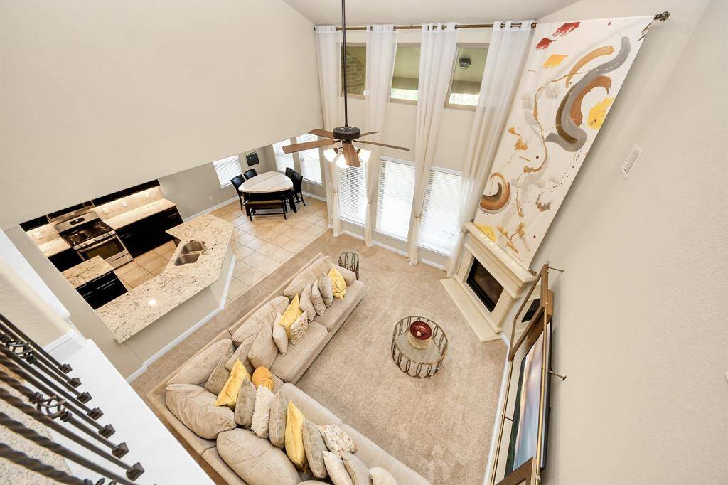 The first floor has an open-concept living area with high ceilings and large windows which make the room feel even larger than it is. It features a cozy seating arrangement around a fireplace, modern kitchen with granite countertops, and an adjacent dining area. A ceiling fan and contemporary artwork add a stylish touch.