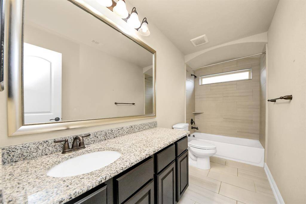 Bathroom #3 features a long granite countertop, a single sink, and dark cabinetry. The room is well-lit with overhead lighting and includes a bathtub/shower combo. The strategically placed window adds natural light.